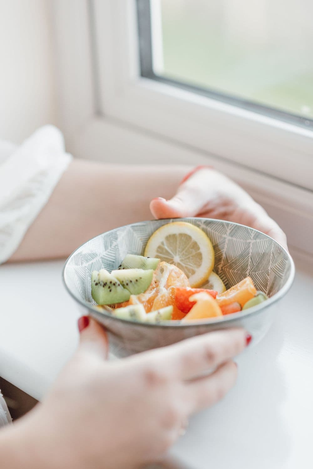 Patiente tenant un bol de fruits frais près d'une fenêtre